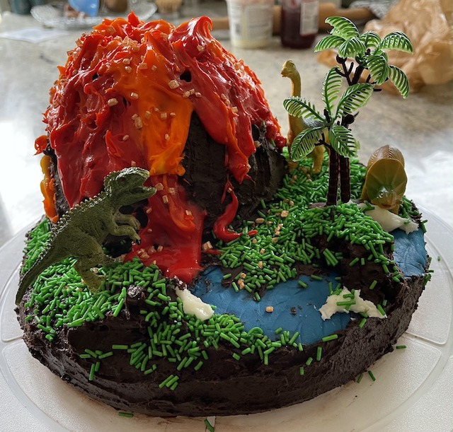 A chocolate cake with red volcano icing, blue river icing and green sprinkles for grass. Plus some borrowed dinosaurs and plastic ferns for decoration
