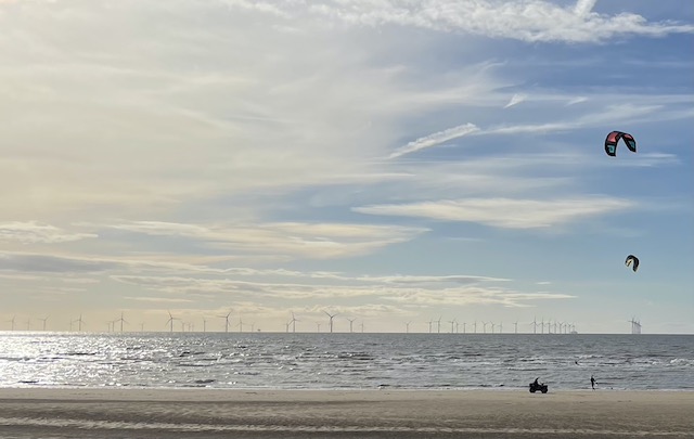 kitesurfers on the sea, with a wind farm in the background, further out to sea.