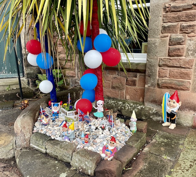 A red, white and blue balloon and flag display outside of a home, with several gnomes.