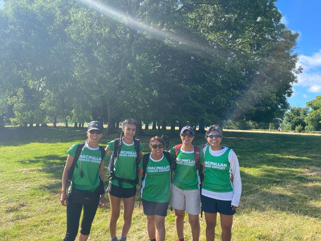 Five of us wearing our green Macmillan tops on a grassy field with trees and a blue sky behind