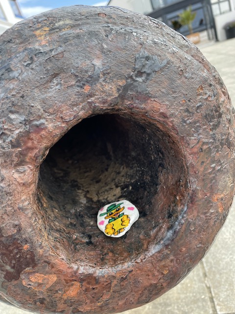 A pebble with a painted duck in a metal cannon mouth