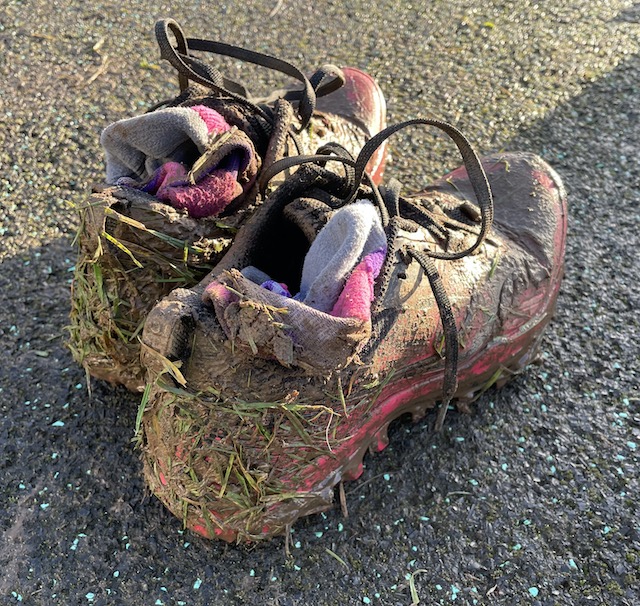 Once pink trail shoes now covered in mud and grass resting on some asphalt ground.