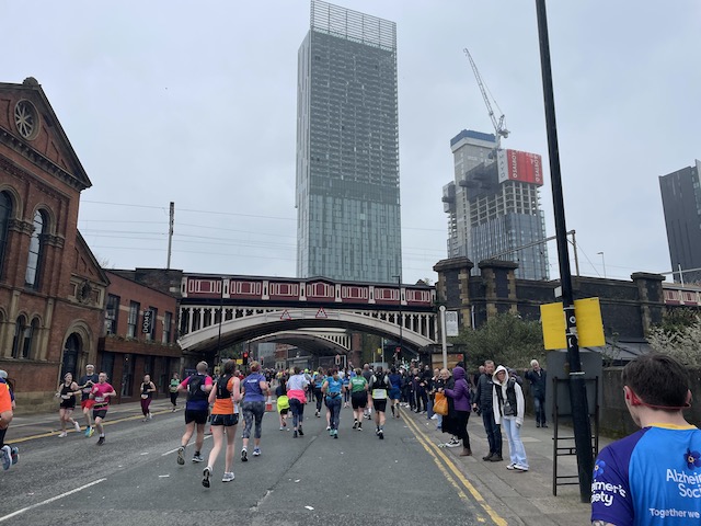 A bridge in the foreground and high rise block in the background with runners streaming on the road