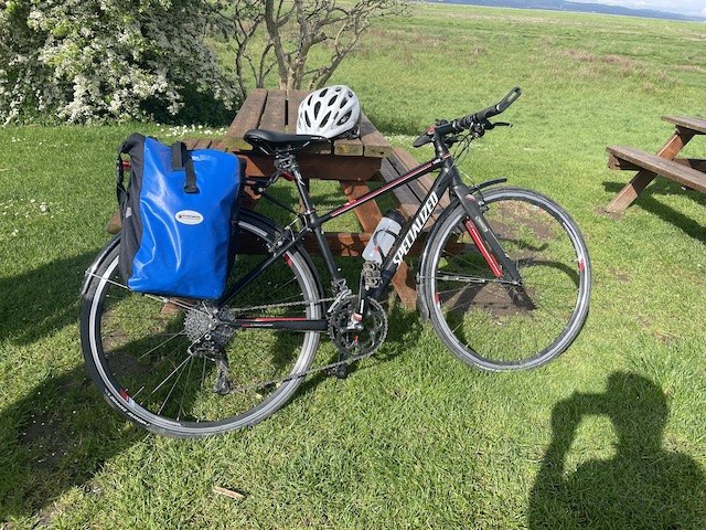Bike with panniers and helmet leaning on a picnic table on the grass in the sun