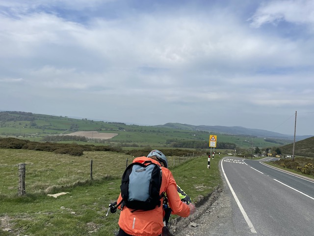 Welsh hills with a few more clouds in the still blue sky, and Sue and her backpack in the near view.
