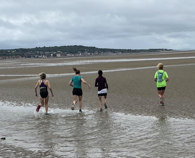 Four women running back to the mainland along the wet sand.