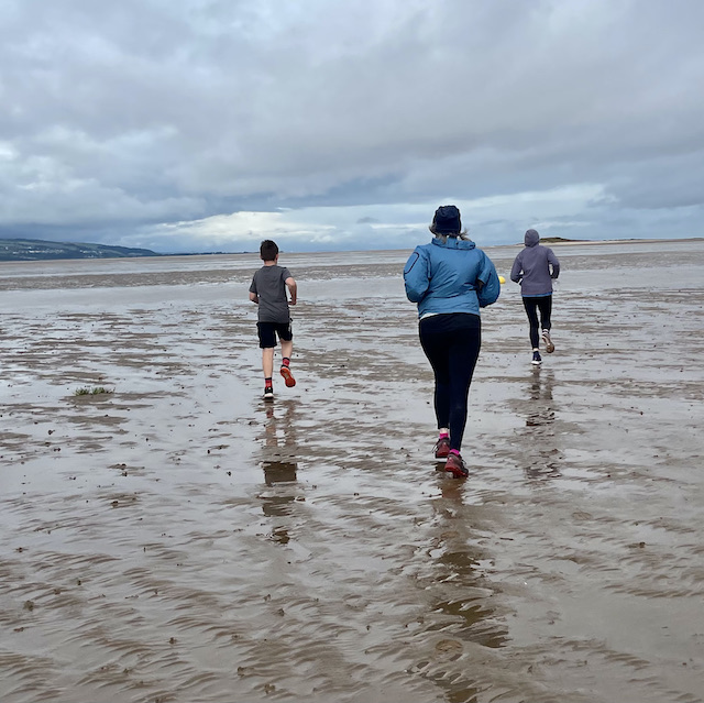 3 people running on wet sand to islands in the distance