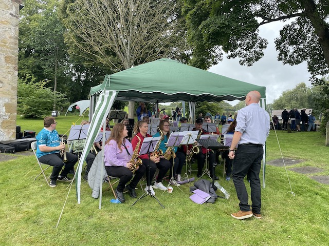 A brass band playing under a green gazebo in a field.