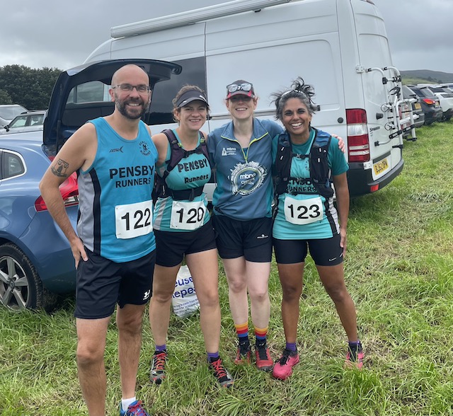 Four runners, including me standing with our Pensby vests in front of parked cars on a field.