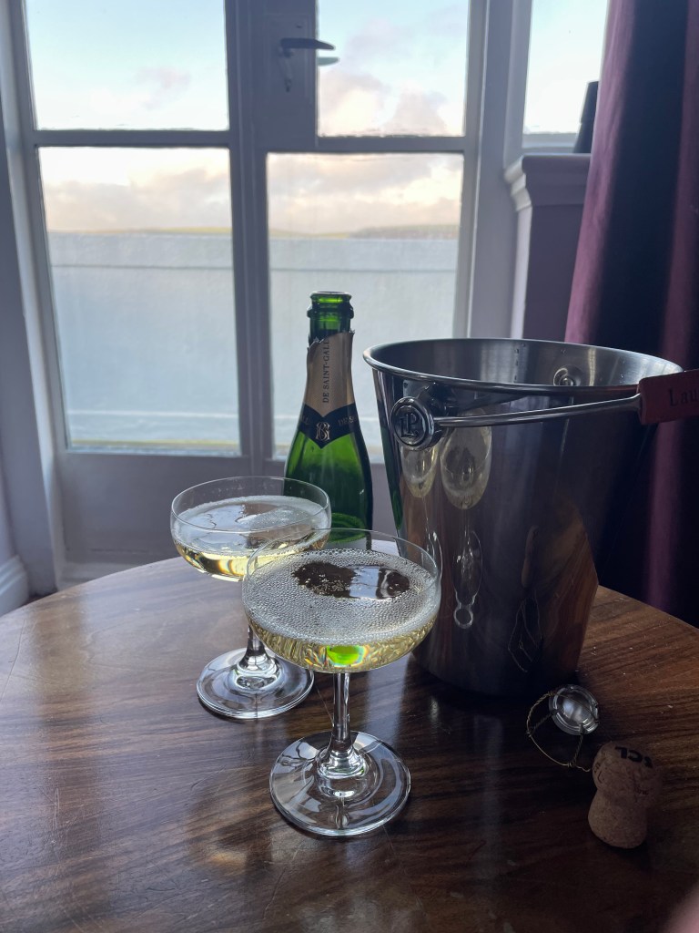 Two glasses filled with champagne on a table with a half-sized bottle of champagne and a cooler bucket. 