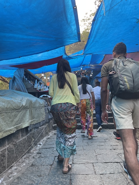 People walking up a path with steps, with covered over stalls and blue makeshift tarpaulin sun protectors.