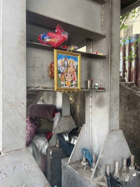 Inside the footings of a bridge are tucked some bundles of clothes and some pots, along with a holy picture.

