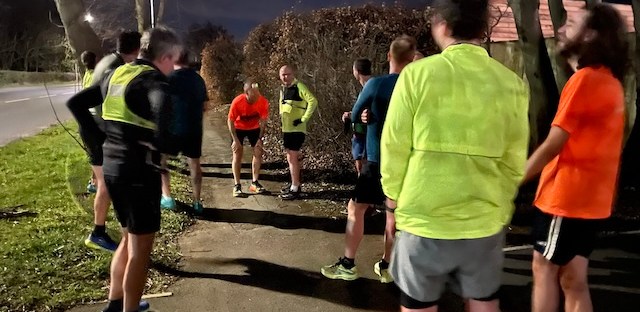 A group of runners standing at the finish line of a night time handicap race.