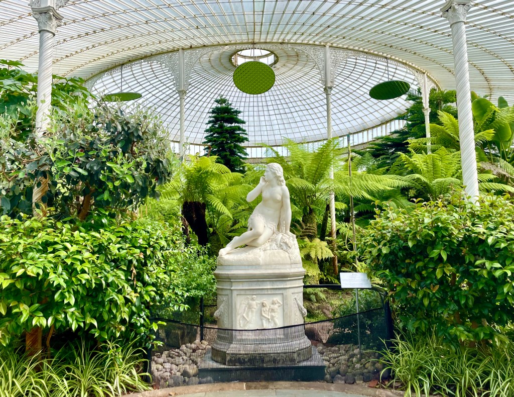 Inside Kibble Palace: marble statue of a naked woman, surrounded by large green plants, with a glass and iron ceiling