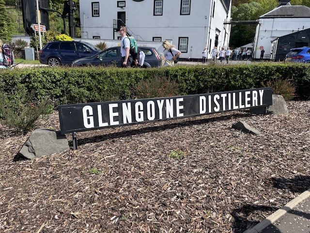 Sign for the Glengoyne Distillery in front of cars and a white building in the background.