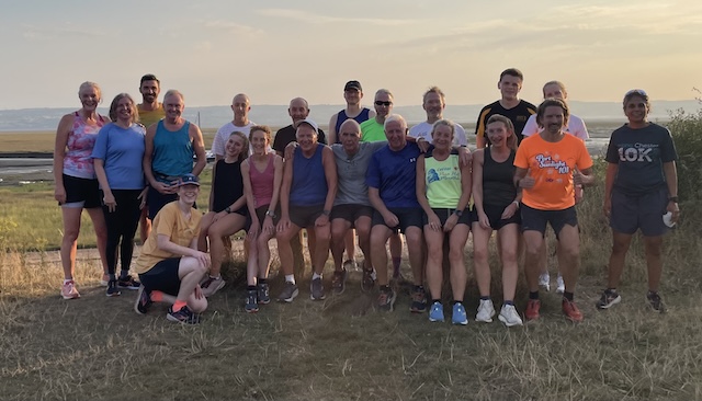 Lots of runners on the grass with the beach and the sea and the evening sky behind them.