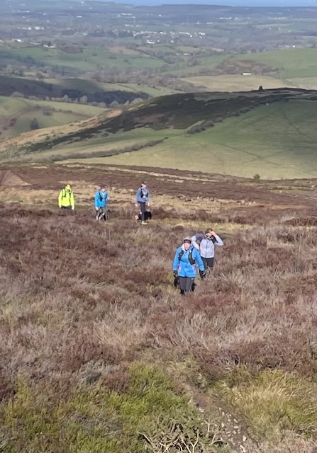 Brown heather in foreground with several colourful runners threading their way through. Hills and towns in background.
