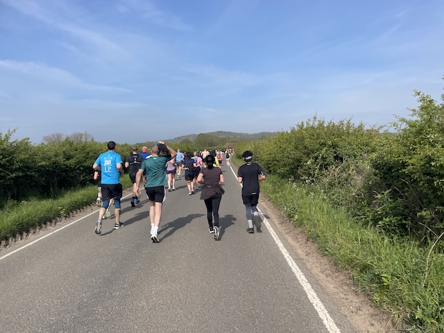 Runners on a road with blue skies and greenery on each side