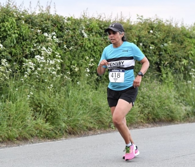 Me, with a concentrated look, trying to run on the road, a high green hedge in the background with white flowers in it.