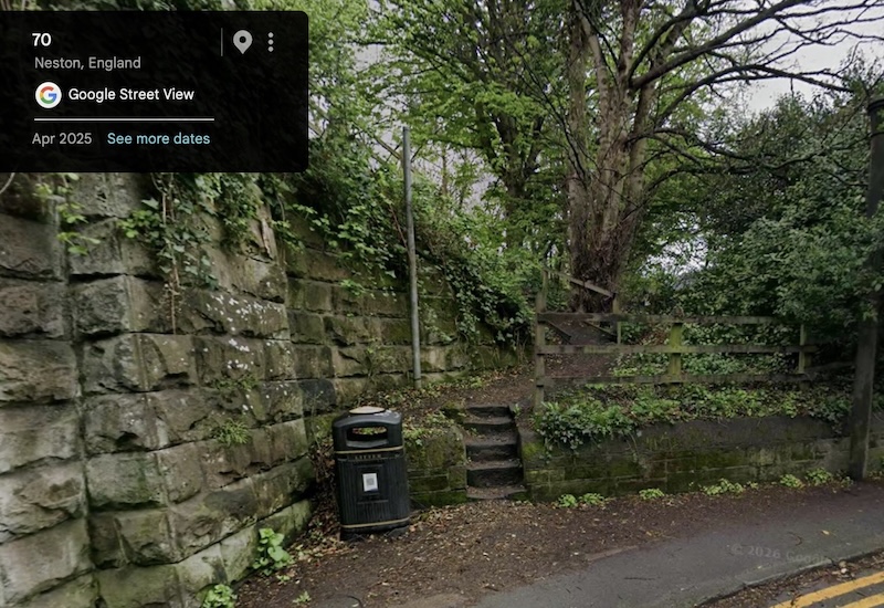On the left the stone wall of a bridge. In front a bin next to a few steps leading to a path, and a tree a bit further back.